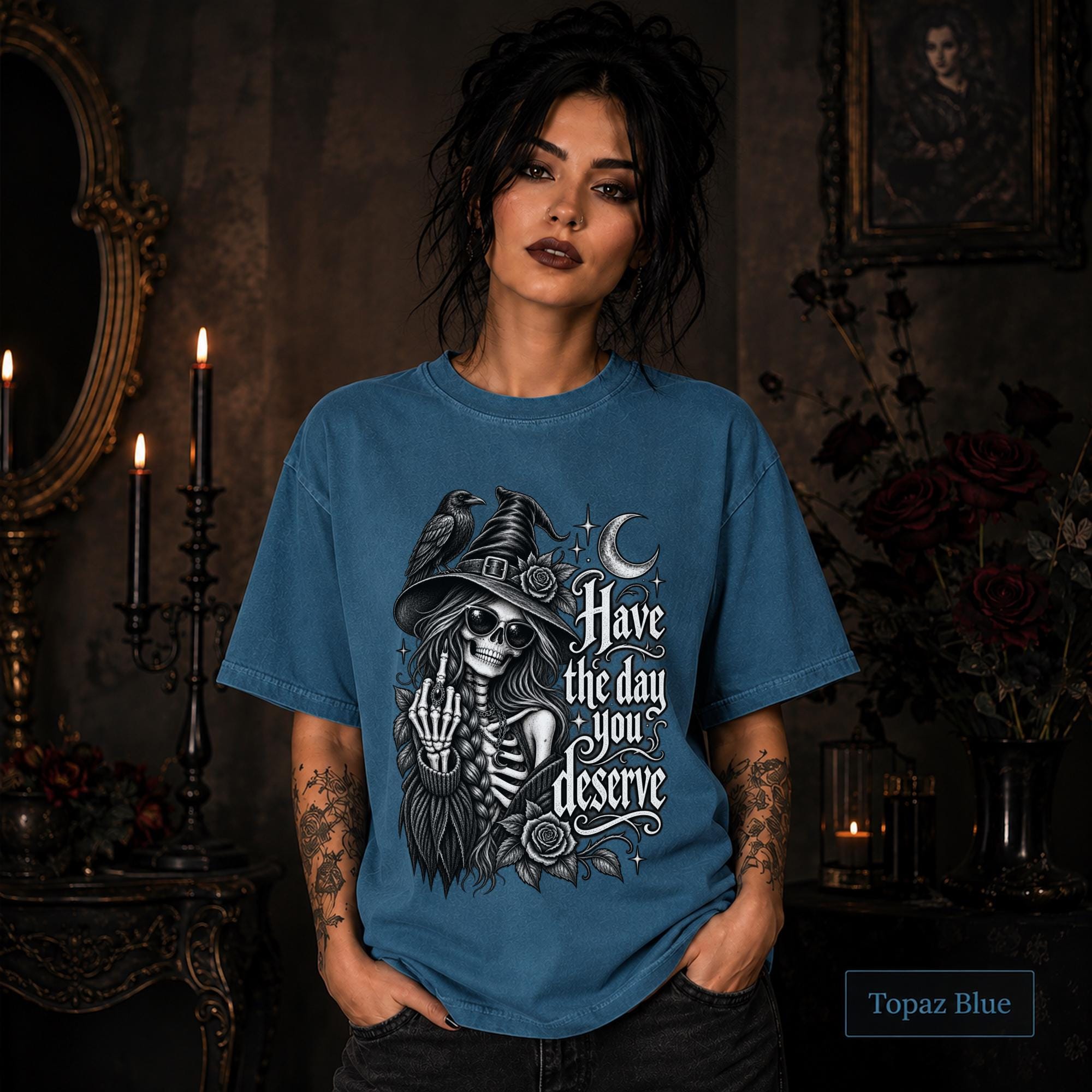 Woman wearing a Topaz blue gothic shirt featuring a skeleton witch, raven, crescent moon, roses, and Have the Day You Deserve text.