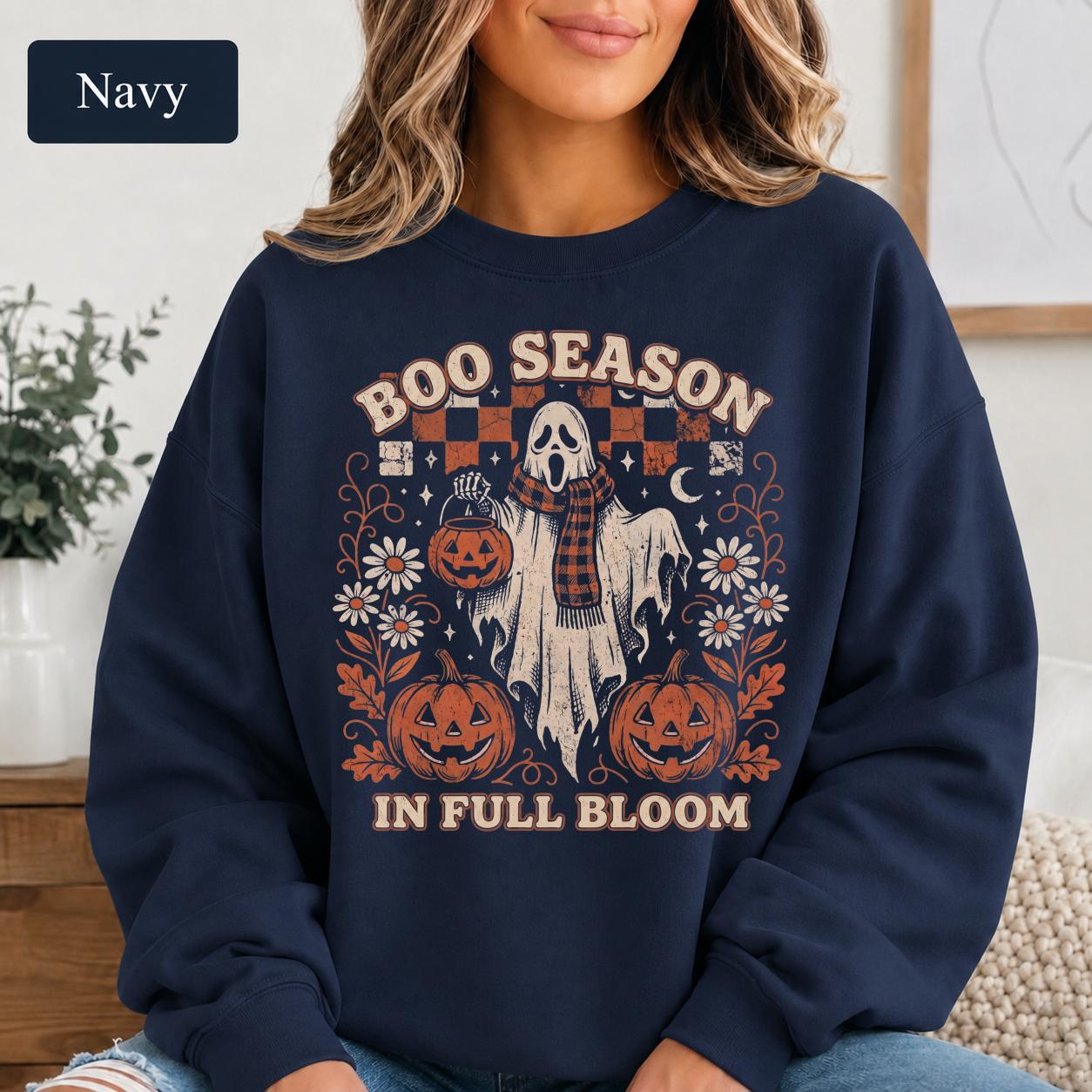 Retro Halloween sweatshirt with cream ghost, orange pumpkins, daisies, checkerboard accents, and fall leaves.