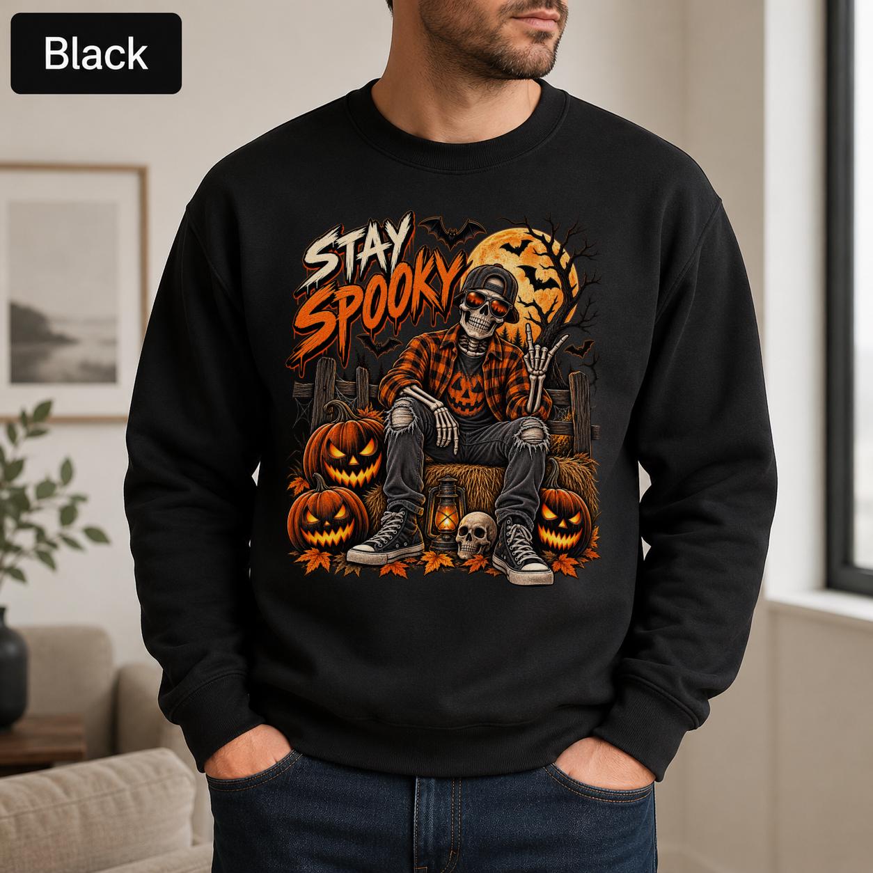 Black Halloween sweatshirt featuring a Stay Spooky skeleton graphic with jack-o’-lanterns, full moon, bats, autumn leaves, and orange fall details.