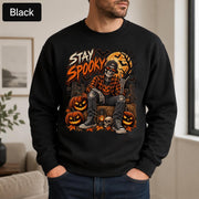 Black Halloween sweatshirt featuring a Stay Spooky skeleton graphic with jack-o’-lanterns, full moon, bats, autumn leaves, and orange fall details.