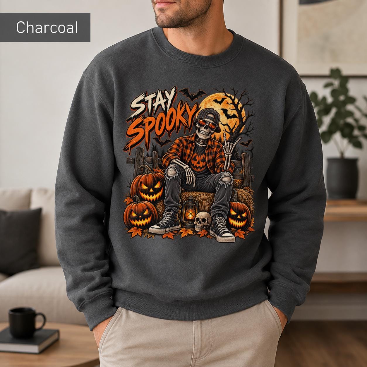 Charcoal Halloween sweatshirt featuring a Stay Spooky skeleton graphic with jack-o’-lanterns, full moon, bats, autumn leaves, and orange fall details.