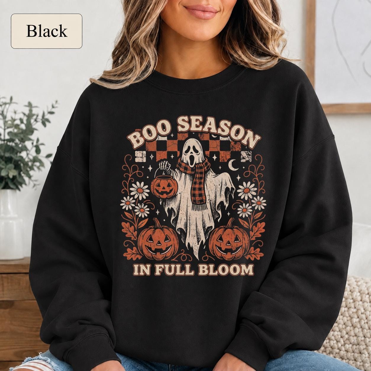 Woman wearing a black Boo Season in Full Bloom Halloween sweatshirt with ghost, pumpkins, flowers, and retro artwork.