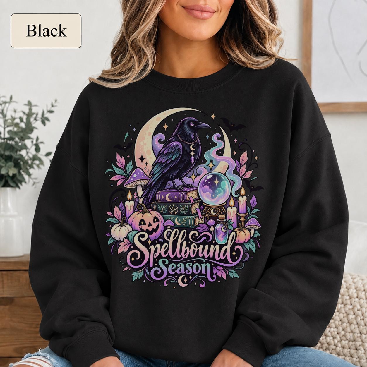 Black Spellbound Season sweatshirt featuring a purple raven, crystal ball, crescent moon, spell books, candles, and pumpkins.