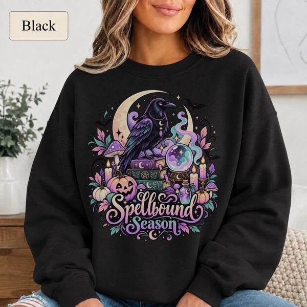 Black Spellbound Season sweatshirt featuring a purple raven, crystal ball, crescent moon, spell books, candles, and pumpkins.