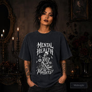 Mental Health Matters midnight T-shirt featuring a seated skeleton, flowers, butterflies, and bold gothic lettering in a monochrome design.