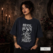 Mental Health Matters navy T-shirt featuring a seated skeleton, flowers, butterflies, and bold gothic lettering in a monochrome design.