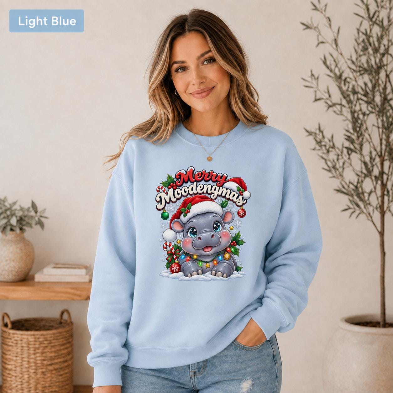 Light blue Christmas sweatshirt featuring a cute hippo in a Santa hat with Merry Moodengmas text, candy canes, ornaments, holly, and snowflakes.