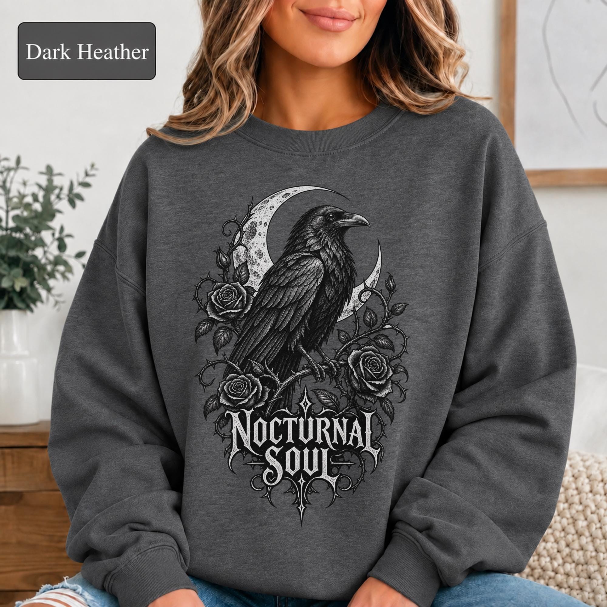 Woman wearing a dark heather crewneck sweatshirt featuring a detailed black raven surrounded by a crescent moon, thorny roses, and Nocturnal Soul lettering.