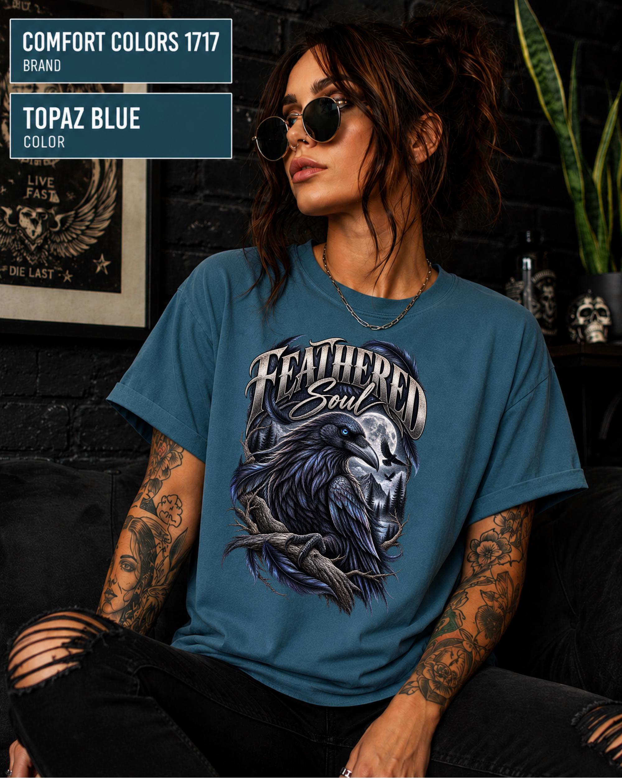 Feathered Soul raven graphic Comfort Colors 1717 T-shirt in topaz blue featuring a detailed black raven with a blue eye, moonlit forest, branches, and gothic artwork.