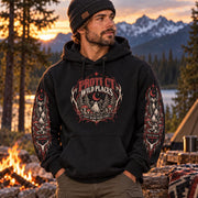 Man wearing a black Protect Wild Places hoodie at a sunset campsite, featuring the front woodland graphic and smaller matching sleeve designs.