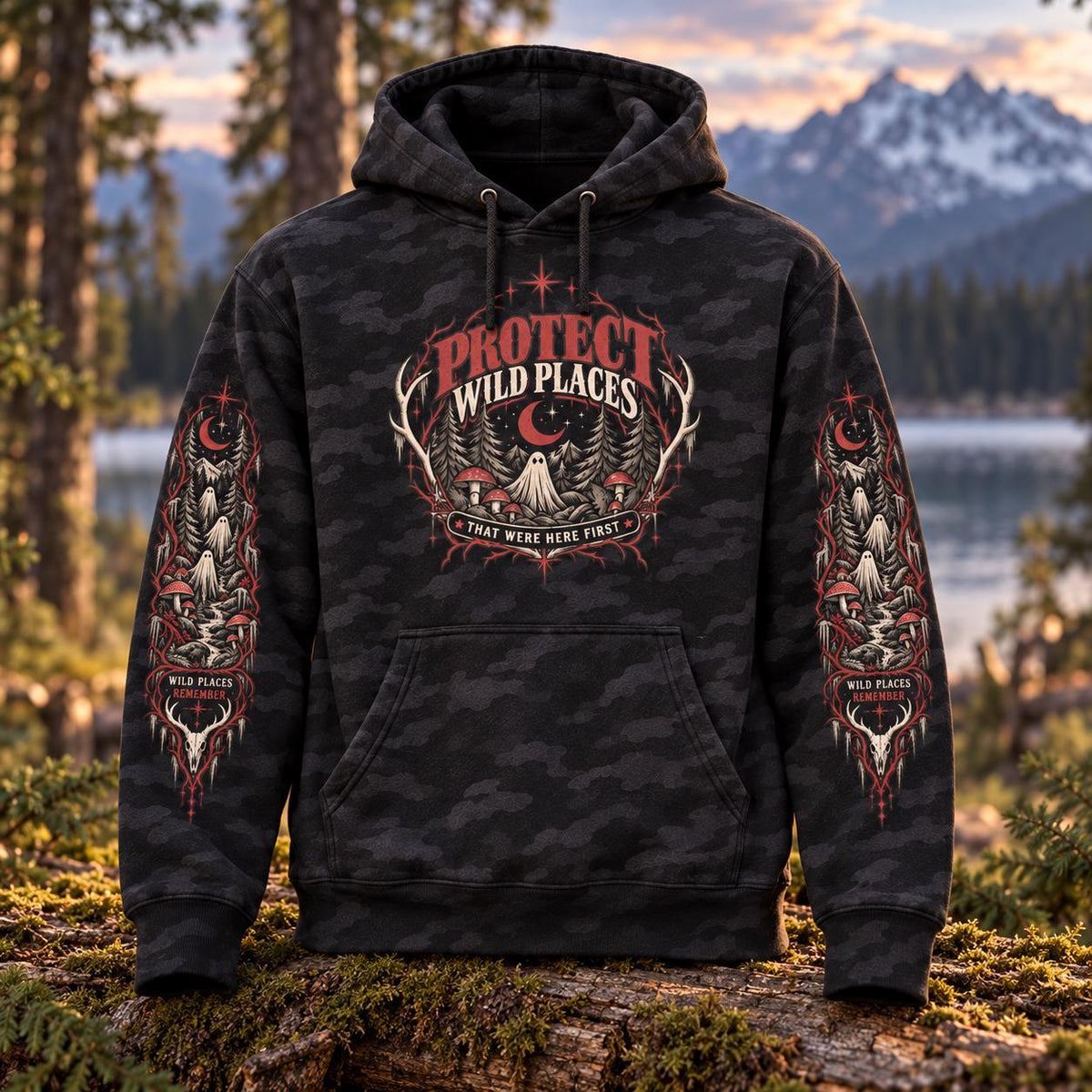 Black camo Protect Wild Places hoodie displayed outdoors in a forest setting, featuring the front graphic and detailed gothic wilderness artwork printed down both sleeves.