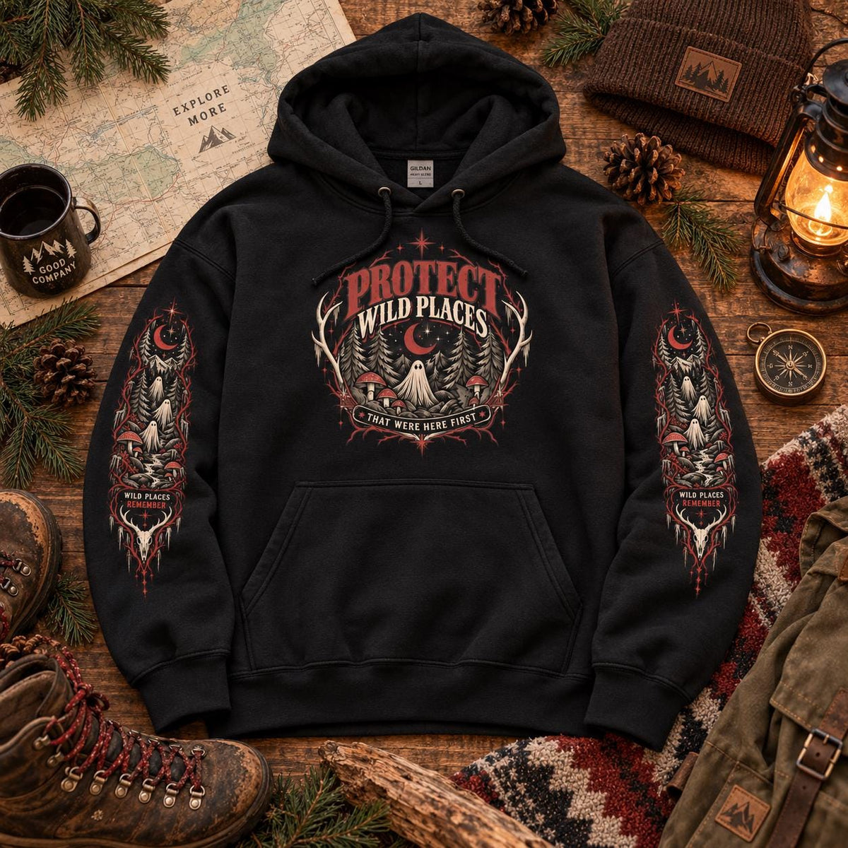 Flat lay of a black Protect Wild Places hoodie with front chest artwork and matching sleeve graphics, styled with hiking boots, map, lantern, and outdoor accessories.