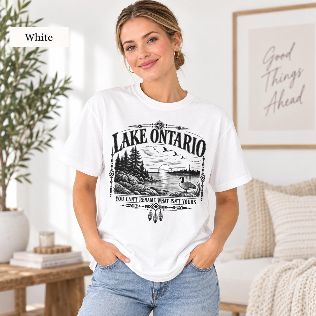 White Comfort Colors Lake Ontario T-shirt featuring a black vintage shoreline design with pine trees, rocky waterfront, Canada goose, Indigenous-inspired geometric details, and the phrase You Can’t Rename What Isn’t Yours.