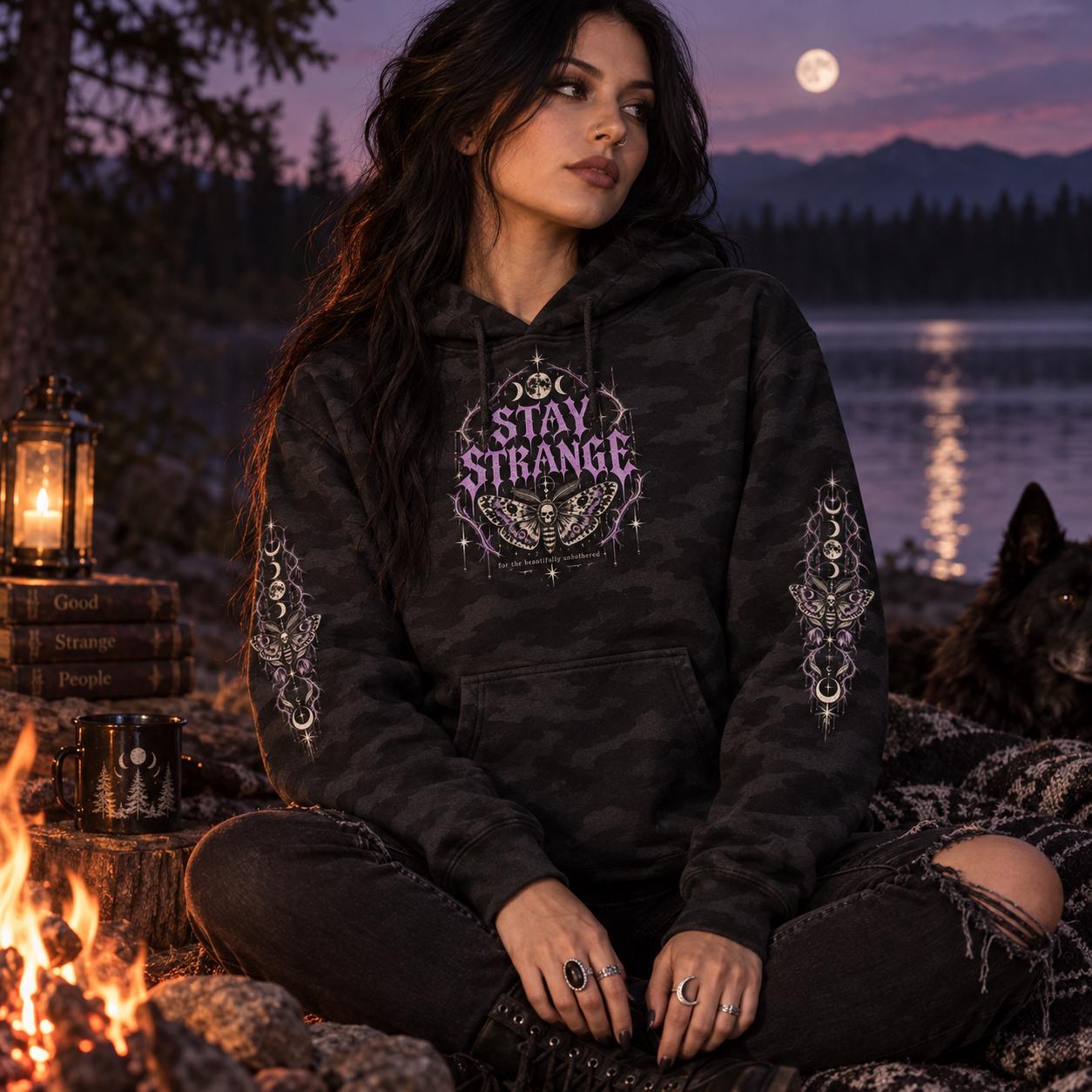 Black camo Stay Strange Social Club heavyweight hoodie featuring purple gothic lettering, death’s-head moth artwork, moon phases, thorn details, and matching celestial sleeve designs.
