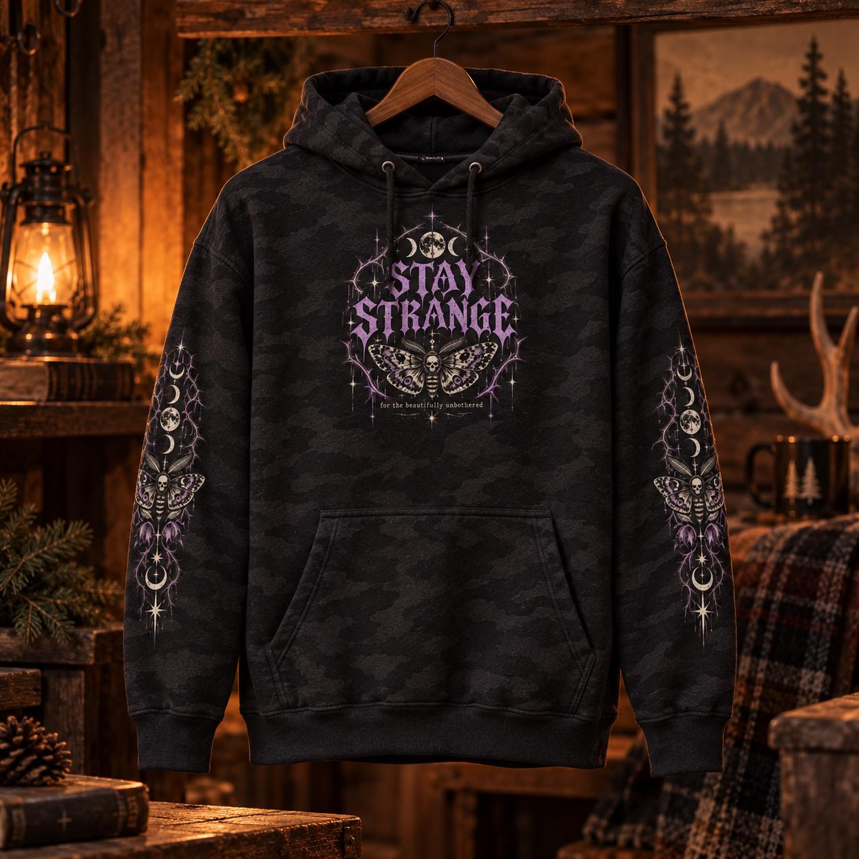 Black camo Stay Strange Social Club heavyweight hoodie featuring purple gothic lettering, death’s-head moth artwork, moon phases, thorn details, and matching celestial sleeve designs.