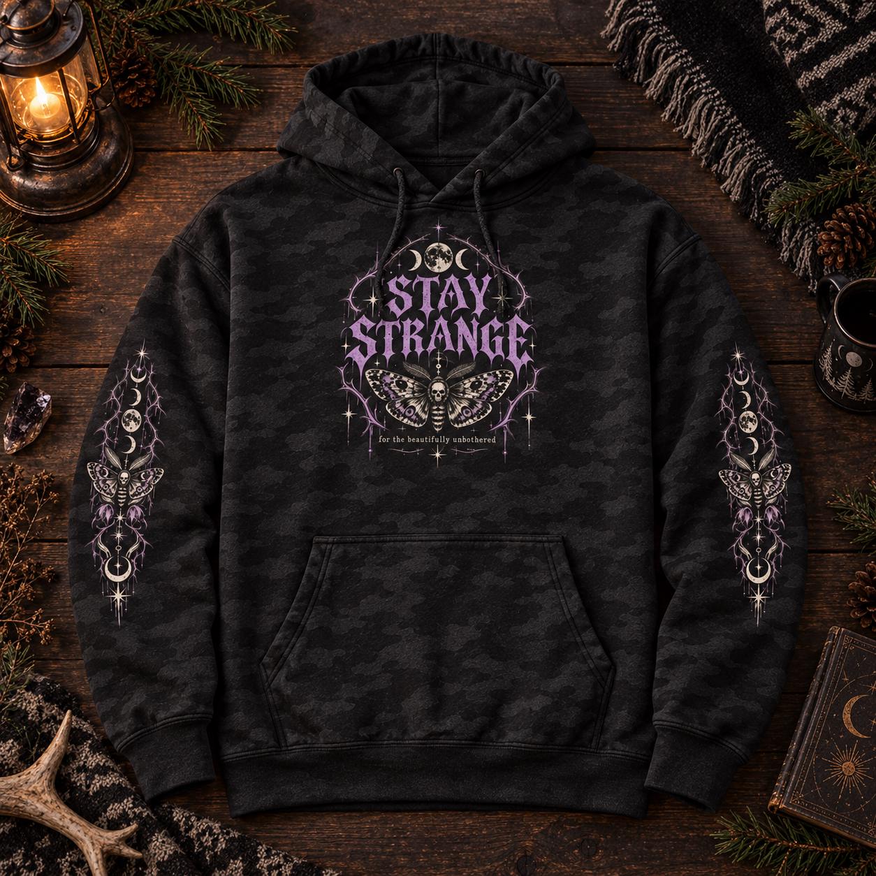 Black camo Stay Strange Social Club heavyweight hoodie featuring purple gothic lettering, death’s-head moth artwork, moon phases, thorn details, and matching celestial sleeve designs.