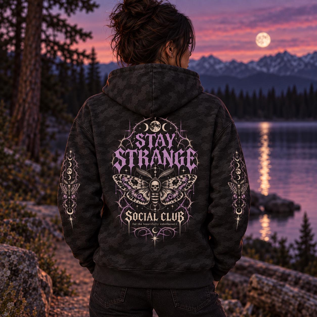 Black camo Stay Strange Social Club heavyweight hoodie featuring purple gothic lettering, death’s-head moth artwork, moon phases, thorn details, and matching celestial sleeve designs.