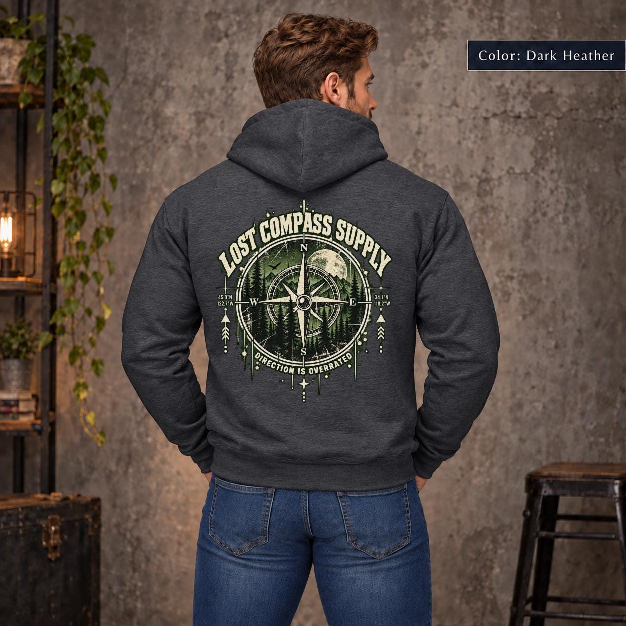 Dark Heather unisex hoodie shown from the back with a large Lost Compass Supply graphic featuring a vintage compass, moonlit forest, directional markings, and the phrase “Direction Is Overrated.”