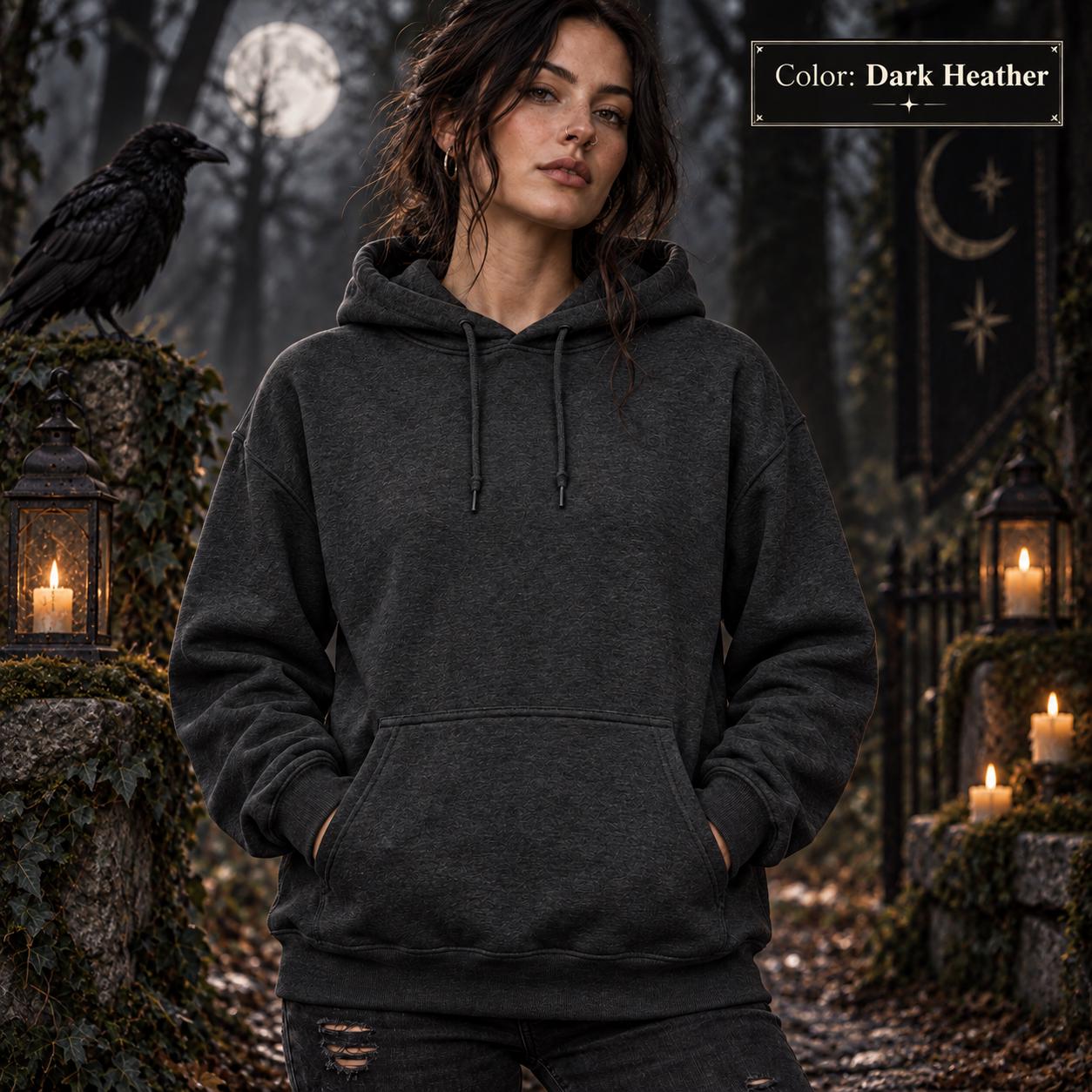 Dark Heather unisex hoodie shown from the front, featuring a large purple raven perched on the back against a glowing violet moon, surrounded by mountains, pine trees, mist, and celestial details.