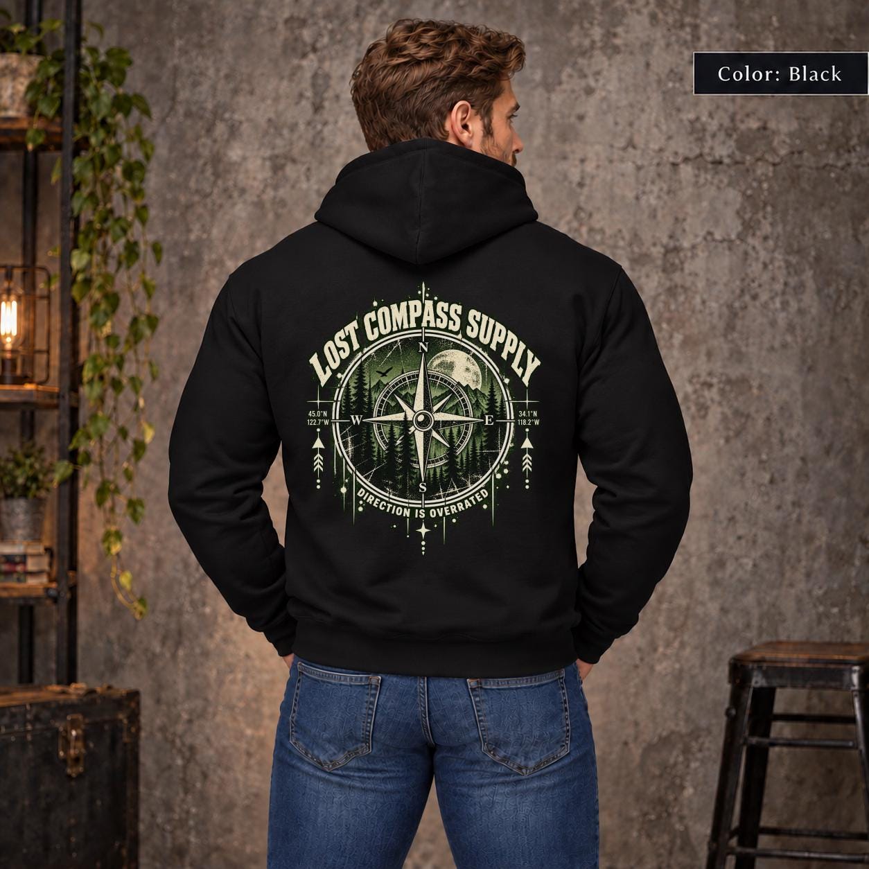 Black unisex hoodie shown from the back with a large Lost Compass Supply graphic featuring a vintage compass, moonlit forest, directional markings, and the phrase “Direction Is Overrated.”