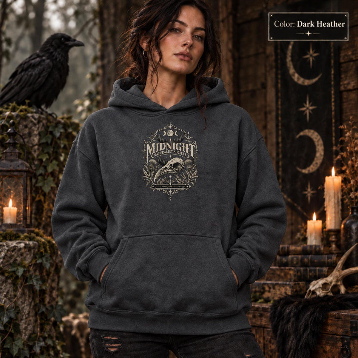 Dark Heather unisex hoodie shown from the front with a smaller Midnight Naturalist Society bird skull emblem centered on the chest in a dark academia inspired style.