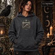 Dark Heather unisex hoodie shown from the front with a smaller Midnight Naturalist Society bird skull emblem centered on the chest in a dark academia inspired style.