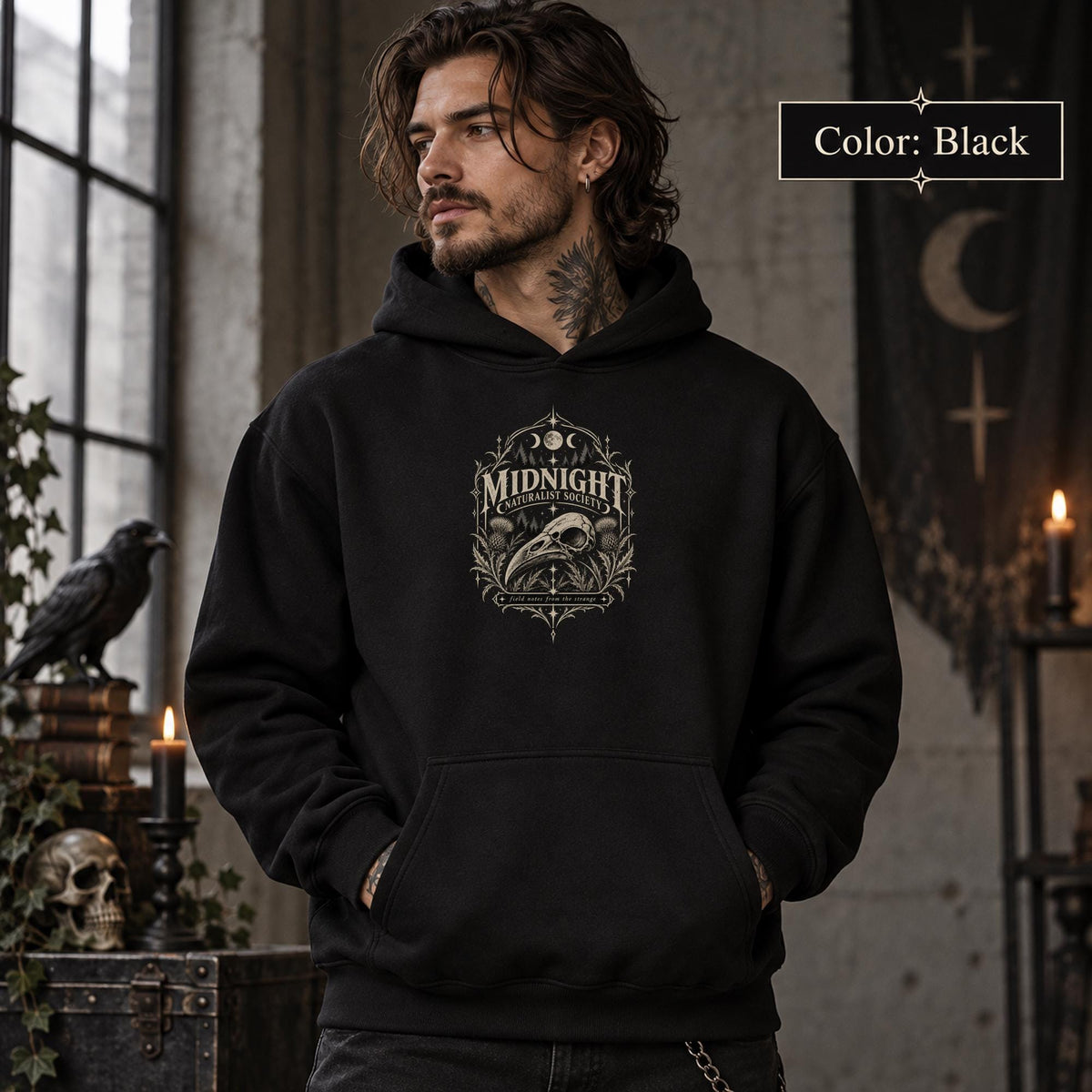 Black unisex hoodie shown from the front with a smaller Midnight Naturalist Society bird skull emblem centered on the chest in a dark academia inspired style.