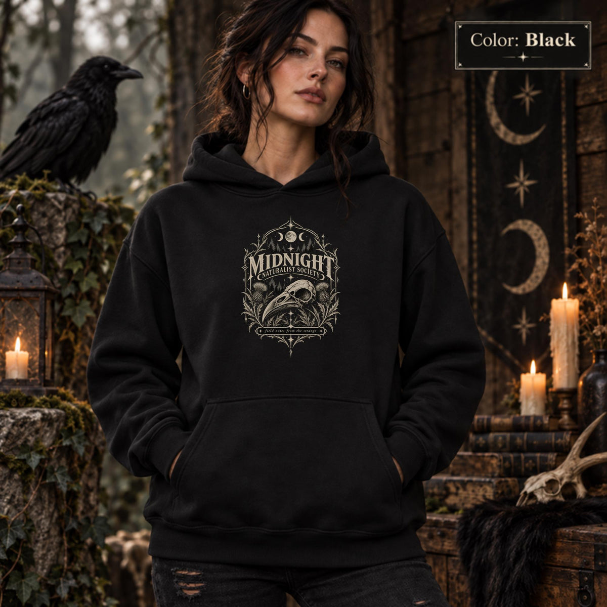 Black unisex hoodie shown from the front with a smaller Midnight Naturalist Society bird skull emblem centered on the chest in a dark academia inspired style.