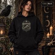 Black unisex hoodie shown from the front with a smaller Midnight Naturalist Society bird skull emblem centered on the chest in a dark academia inspired style.