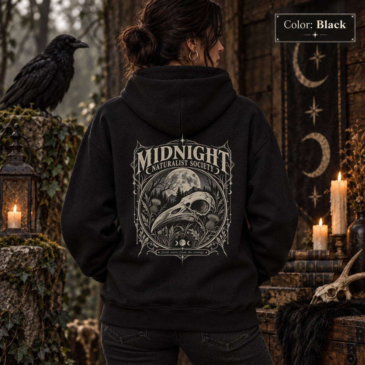 Black Black unisex hoodie shown from the back with a large Midnight Naturalist Society graphic featuring a bird skull, moon, mountains, forest plants, and vintage gothic botanical details.