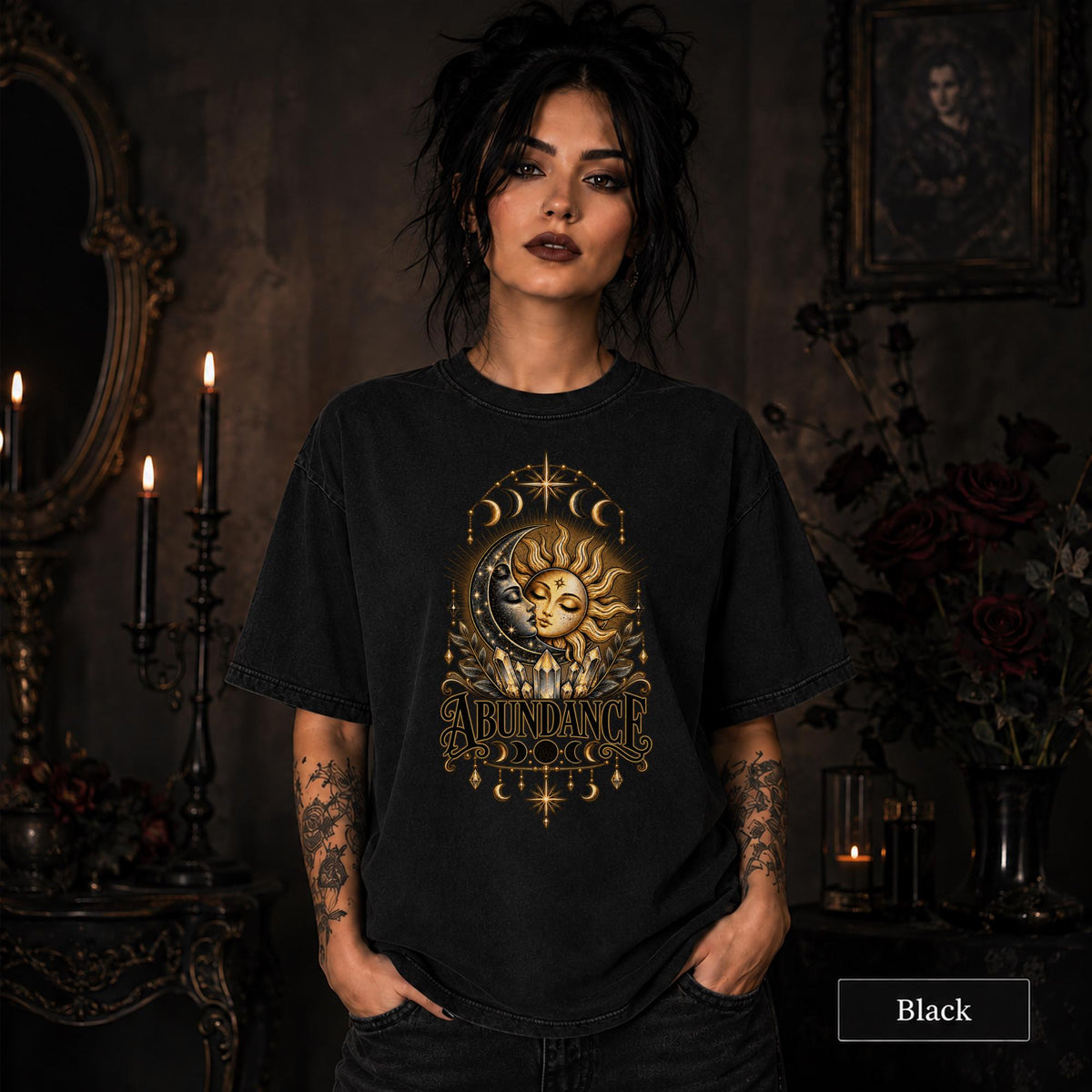 Female model wearing a black Comfort Colors 1717 shirt with a gold celestial Abundance design featuring sun and moon faces, crystals, stars, and moon phases.