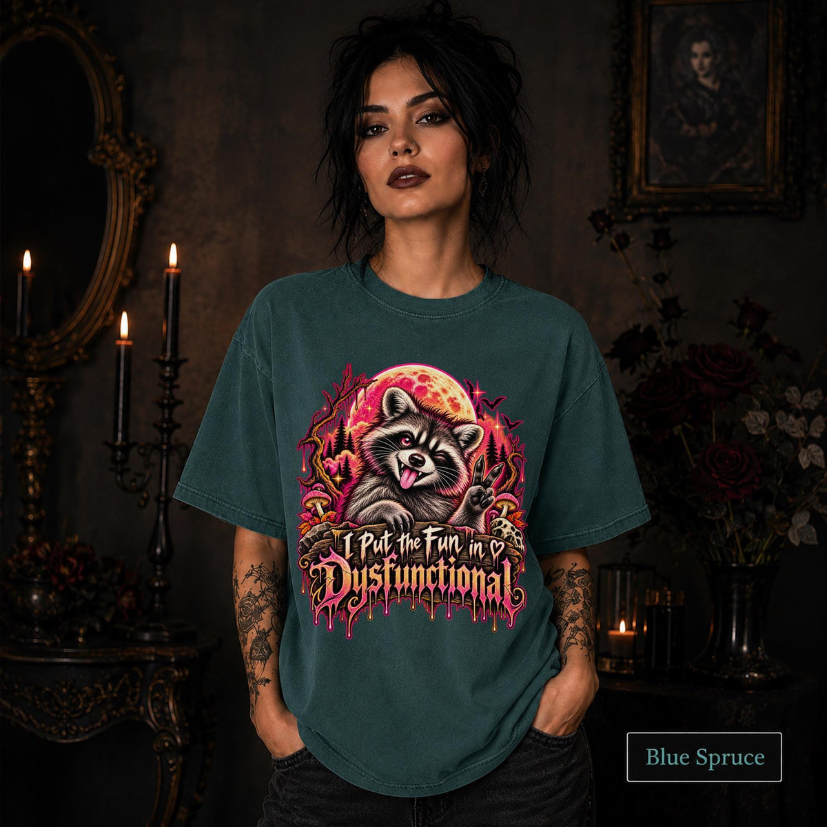 Female model wearing a blue spruce Comfort Colors 1717 tee featuring a colorful raccoon beneath a glowing moon with mushrooms and the phrase “I Put the Fun in Dysfunctional.”