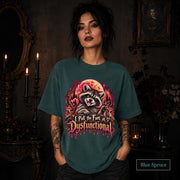 Female model wearing a blue spruce Comfort Colors 1717 tee featuring a colorful raccoon beneath a glowing moon with mushrooms and the phrase “I Put the Fun in Dysfunctional.”