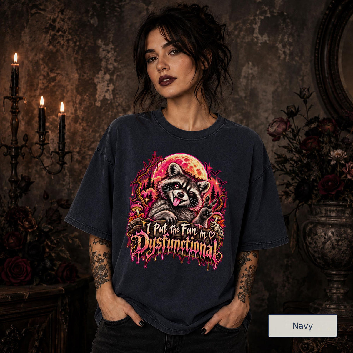 Female model wearing a navy Comfort Colors 1717 tee featuring a colorful raccoon beneath a glowing moon with mushrooms and the phrase “I Put the Fun in Dysfunctional.”