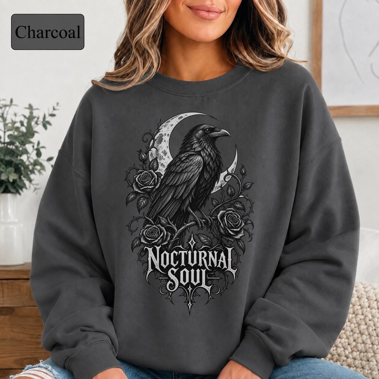 Woman wearing a charcoal crewneck sweatshirt featuring a detailed black raven surrounded by a crescent moon, thorny roses, and Nocturnal Soul lettering.