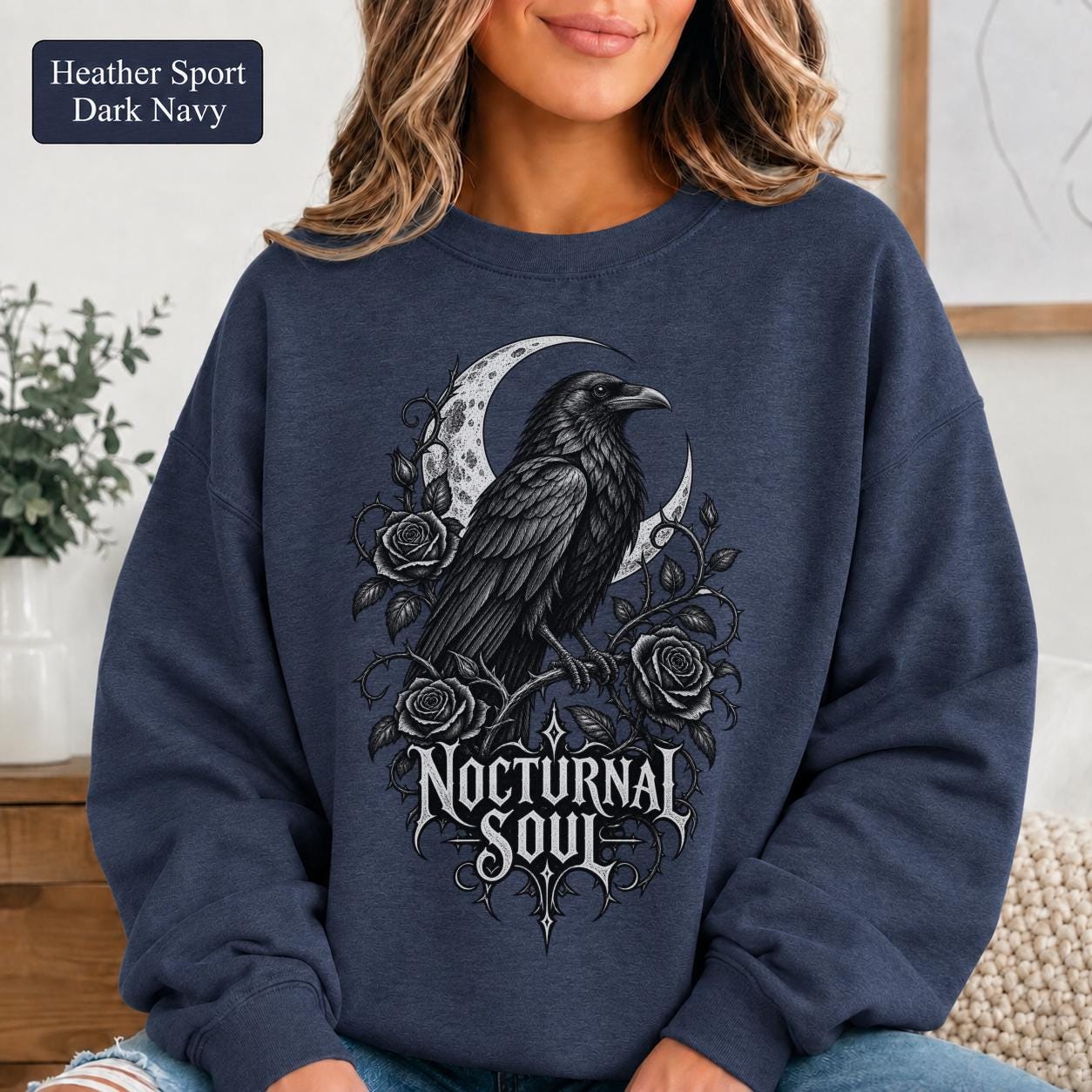 Woman wearing a heather sport dark navy crewneck sweatshirt featuring a detailed black raven surrounded by a crescent moon, thorny roses, and Nocturnal Soul lettering.