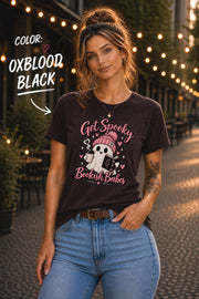 Get Spooky Bookish Babes T-shirt featuring a cute ghost in a pink beanie holding a book and coffee, with hearts and stars on a Oxblood Black shirt.