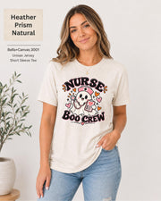 Nurse Boo Crew T-shirt in Heather Prism Natural featuring a cute ghost nurse with a pink cap, stethoscope, clipboard, hearts, and playful Halloween accents.