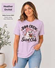 Boo Crew Social Club T-shirt in Heather Orchid featuring a cute ghost in a pink beanie holding books, with hearts, sparkles, and playful Halloween lettering.