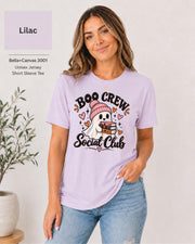 Boo Crew Social Club T-shirt in Lilac featuring a cute ghost in a pink beanie holding books, with hearts, sparkles, and playful Halloween lettering.