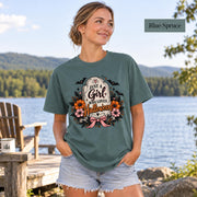 Just a Girl Who Loves Halloween T-shirt in blue spruce featuring a floral tombstone design with bats, orange and pink flowers, hearts, sparkles, and a pink bow.