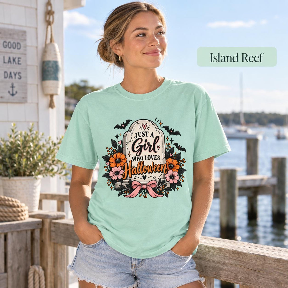 Just a Girl Who Loves Halloween T-shirt in island reef featuring a floral tombstone design with bats, orange and pink flowers, hearts, sparkles, and a pink bow.