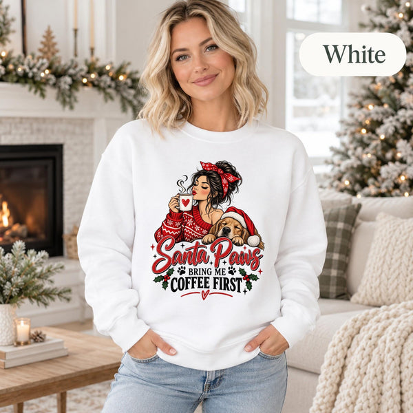 White crewneck sweatshirt featuring a festive “Santa Paws Bring Me Coffee First” design with a woman holding a mug beside a dog in a Santa hat, shown on a female model in a cozy Christmas setting.