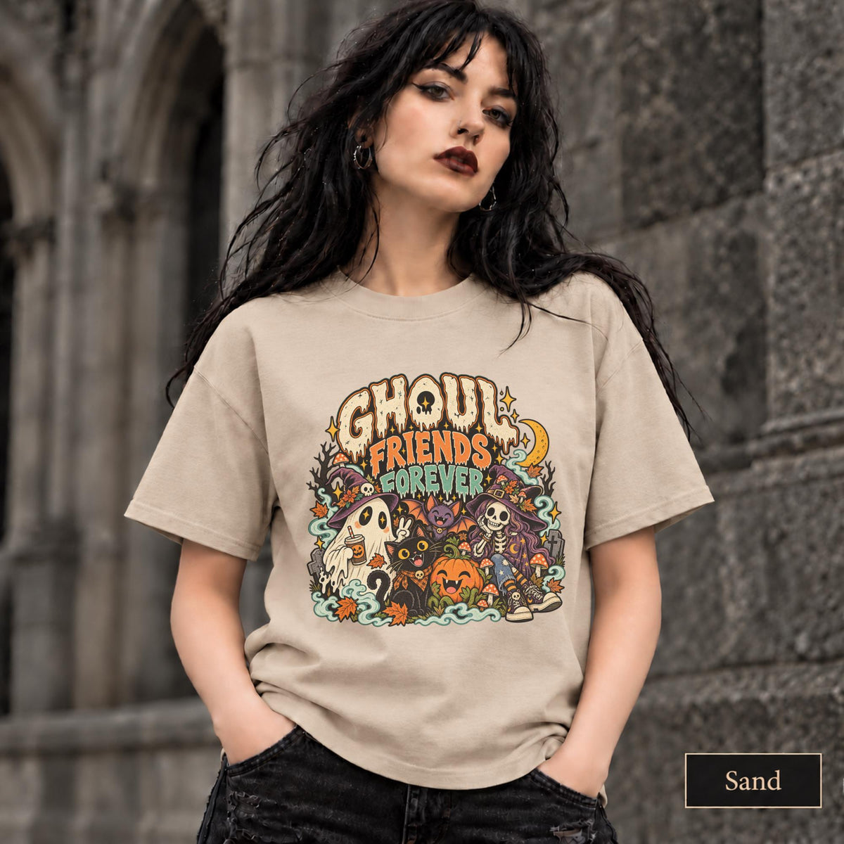 Sand unisex T-shirt featuring a colorful “Ghoul Friends Forever” Halloween graphic with a ghost, black cat, pumpkin, witchy skeleton, bats, mushrooms, crescent moon, and autumn accents.