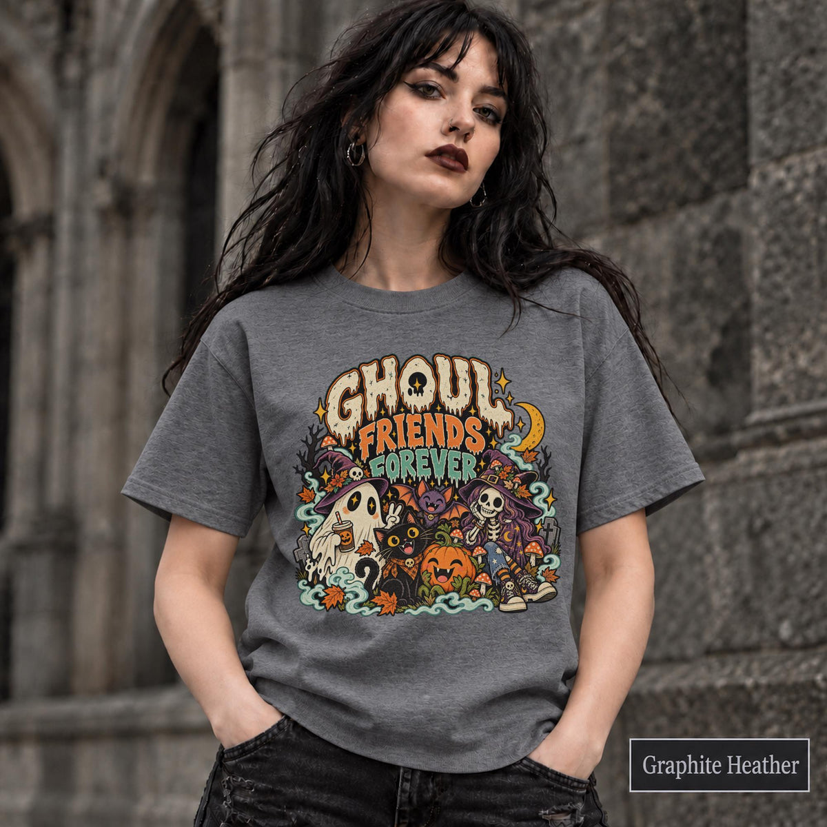 Graphite Heather unisex T-shirt featuring a colorful “Ghoul Friends Forever” Halloween graphic with a ghost, black cat, pumpkin, witchy skeleton, bats, mushrooms, crescent moon, and autumn accents.