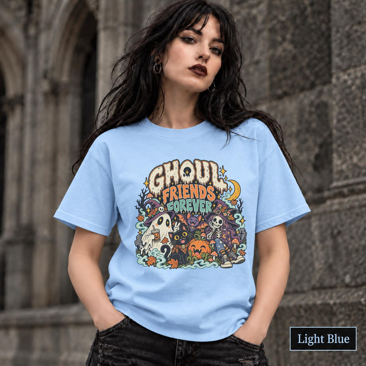 Light Blue unisex T-shirt featuring a colorful “Ghoul Friends Forever” Halloween graphic with a ghost, black cat, pumpkin, witchy skeleton, bats, mushrooms, crescent moon, and autumn accents.