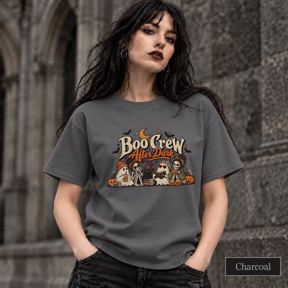 Charcoal unisex T-shirt featuring a “Boo Crew After Dark” Halloween design with ghosts, skeletons, pumpkins, books, bats, drinks, and a crescent moon in retro orange and cream tones.