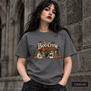 Charcoal unisex T-shirt featuring a “Boo Crew After Dark” Halloween design with ghosts, skeletons, pumpkins, books, bats, drinks, and a crescent moon in retro orange and cream tones.