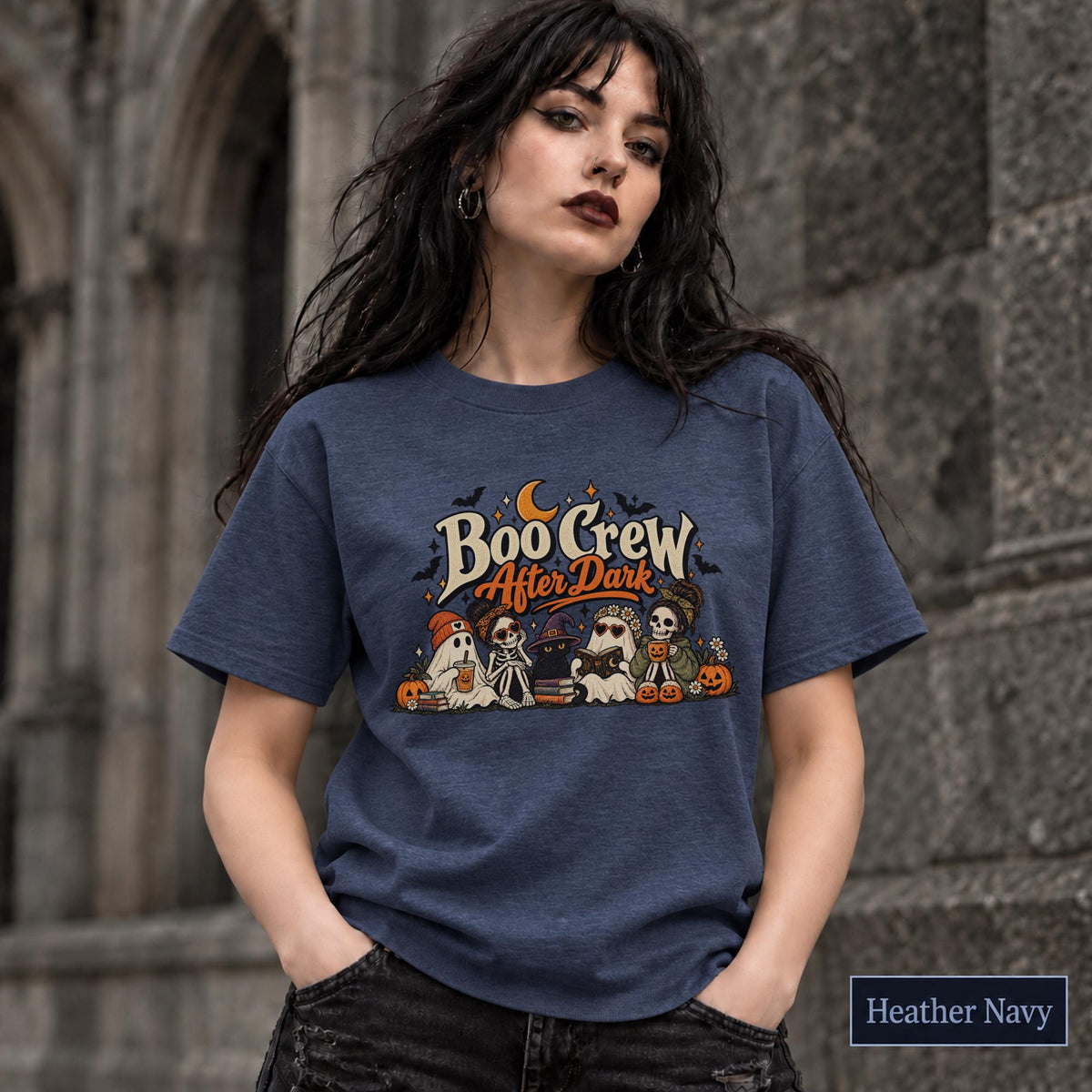 Heather Navy unisex T-shirt featuring a “Boo Crew After Dark” Halloween design with ghosts, skeletons, pumpkins, books, bats, drinks, and a crescent moon in retro orange and cream tones.
