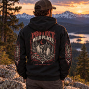 Back view of a man wearing a black Protect Wild Places hoodie at sunset in the mountains, showing the large back graphic with ghosts, trees, mushrooms, and moon details.
